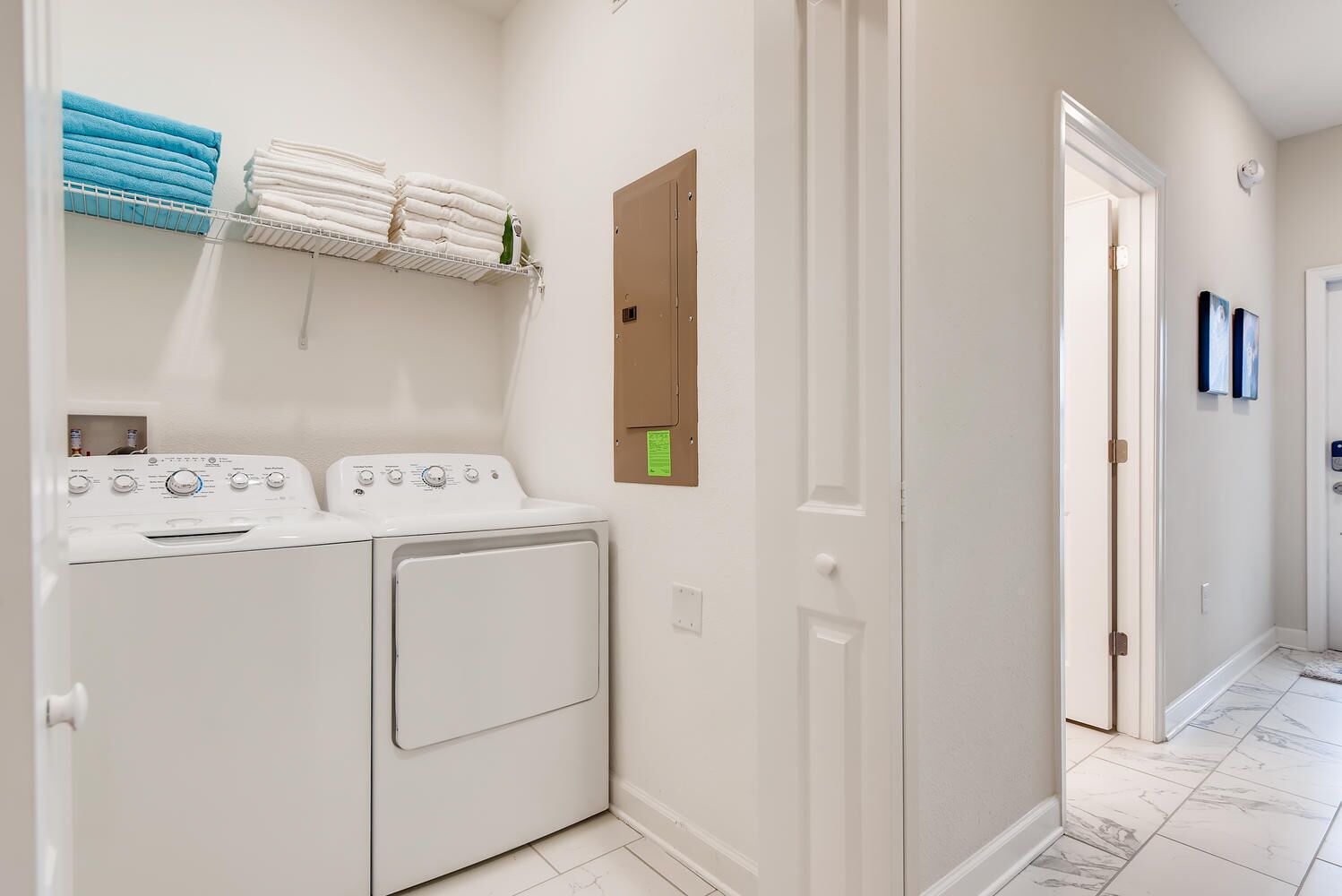 A laundry area with a washing machine and dryer, a towel rack with folded towels, and a door with a bulletin board.