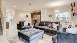 A modern living room with a sectional sofa, ottoman, and a dining area with a table and chairs. - 5BR Villa Bliss: Private Pool - Sleeps 14 - 412 (Davenport)