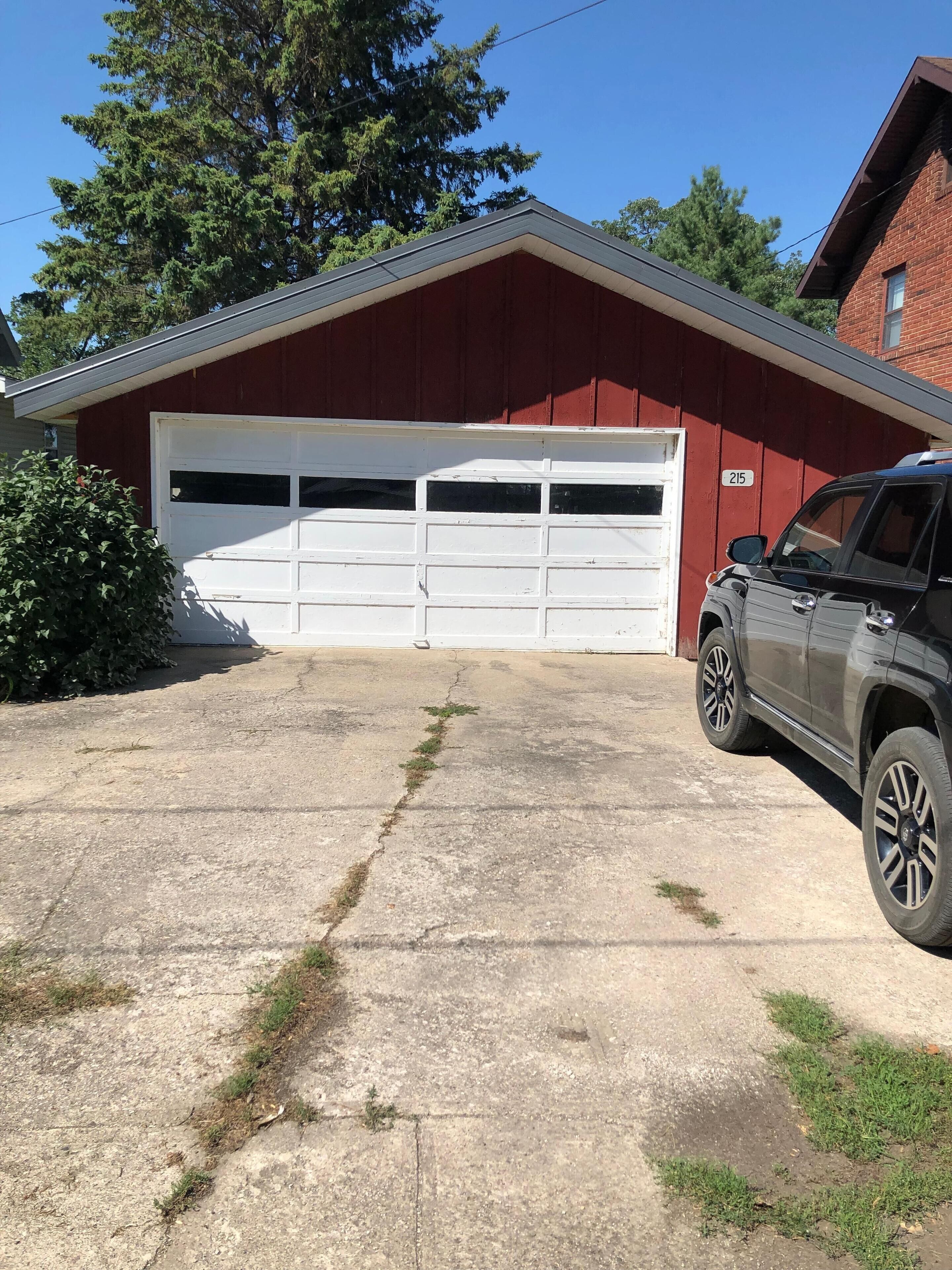 A red garage with a white door, a number 215 on the wall, and a parked SUV.