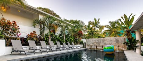 A pool area with lounge chairs, a water feature, and tropical plants.