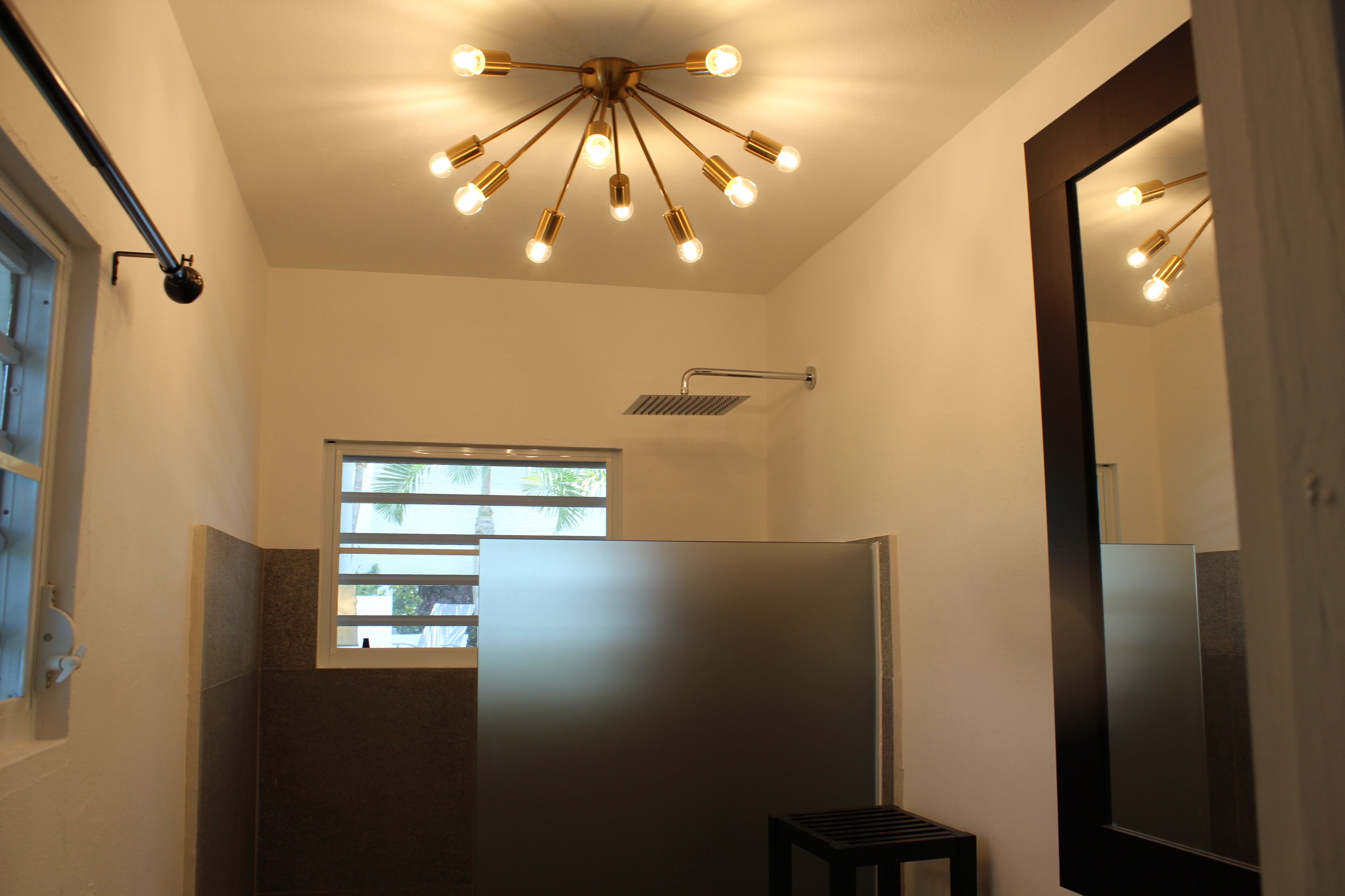 Une salle de bain avec une douche, une fenêtre, un miroir et un luminaire au plafond.