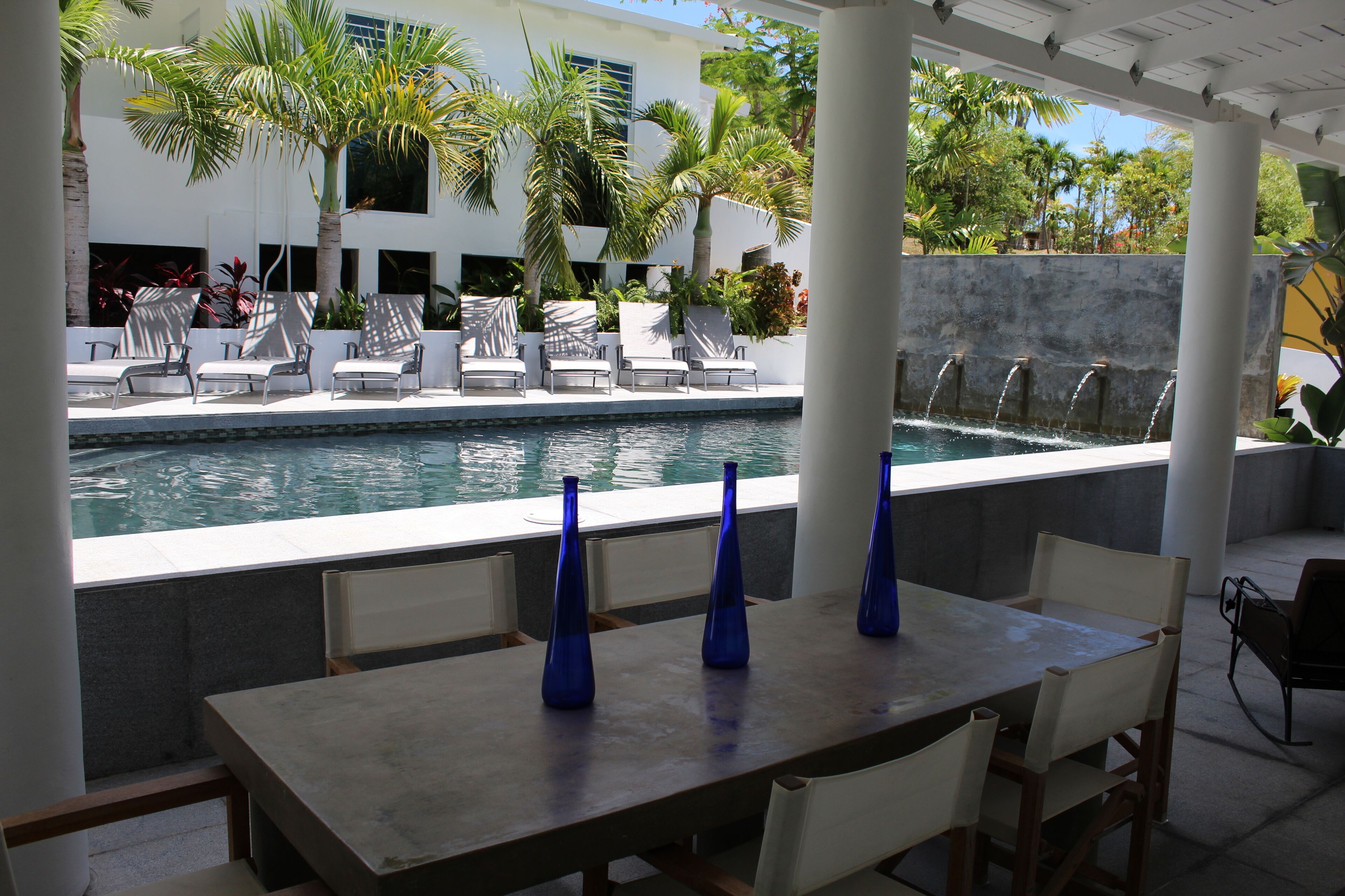 A poolside area with lounge chairs, a table with blue vases, and a water feature.