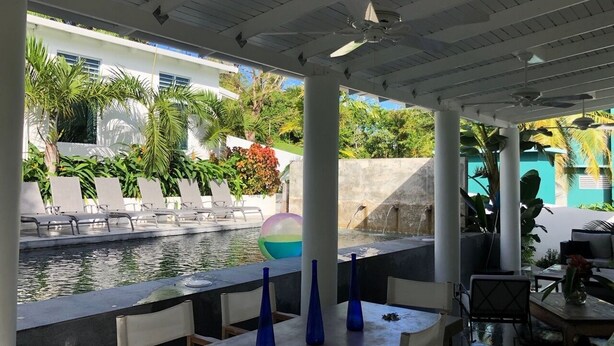 A poolside area with lounge chairs, a pool, and a view of a building with greenery. - Palm Cottages - Entire Compound - Tropical Oasis (Vieques)