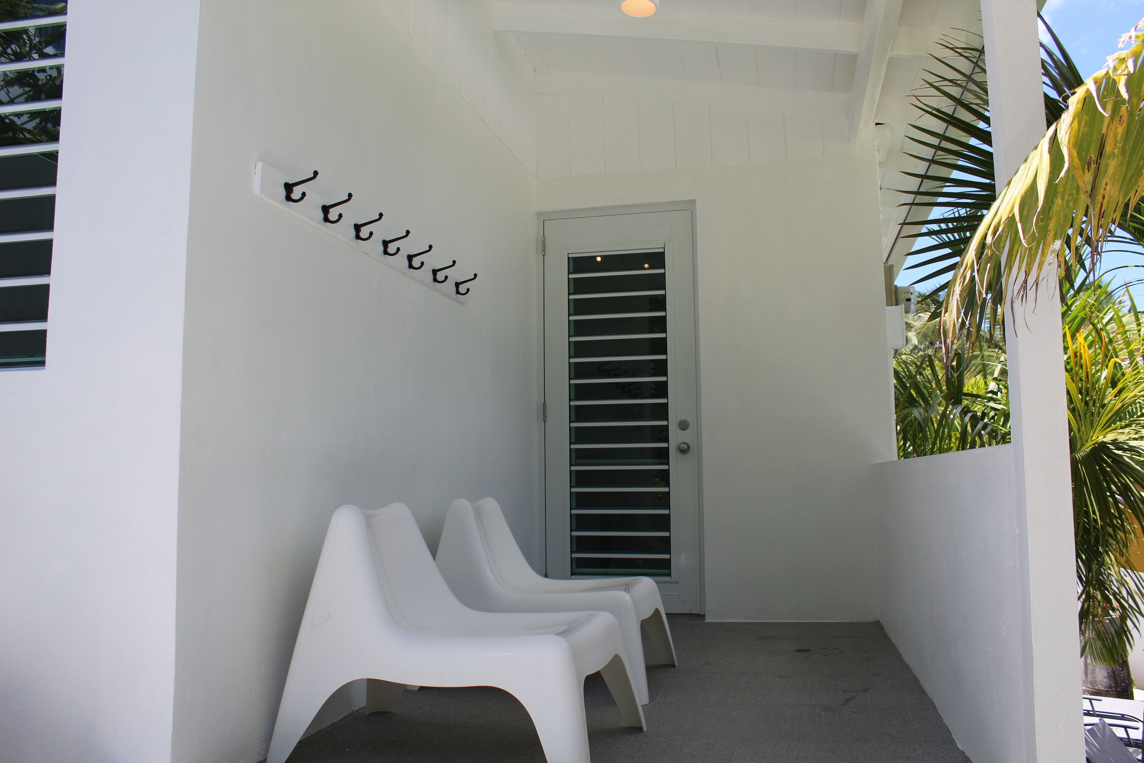 A white exterior wall with a door and a set of white chairs.