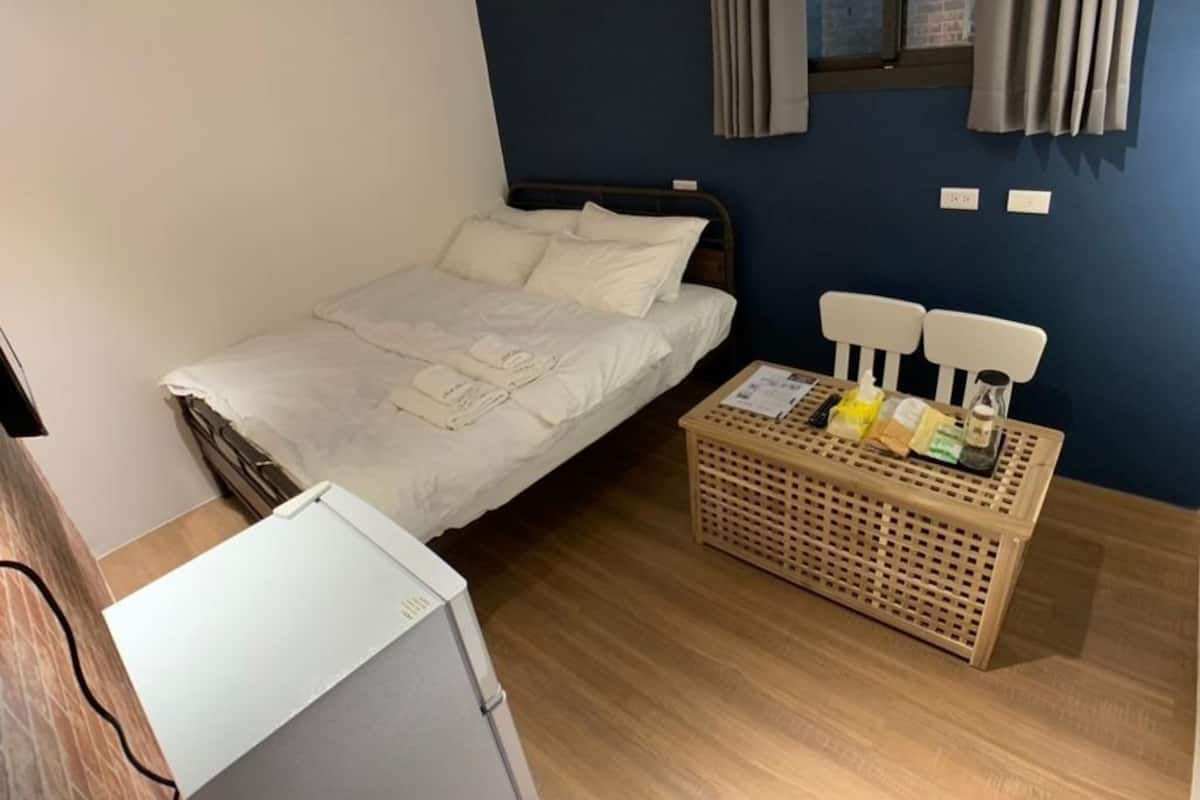 Une chambre à coucher avec un lit, une petite table sur laquelle sont posés des articles de toilette et une fenêtre avec des rideaux.