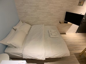 A neatly made bed with white linens in a room with a brick-patterned wall and a mounted flat-screen TV.