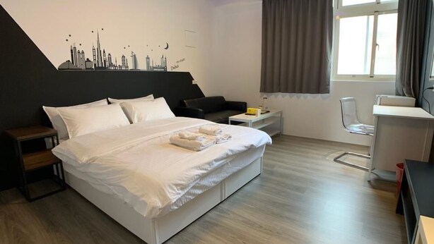 Una habitación de hotel moderna con una cama grande, un escritorio, una silla y un mural con el paisaje urbano en la pared.
