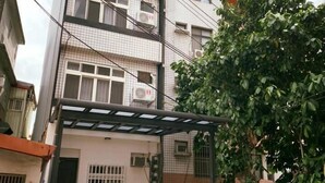 Un edificio residencial de varios pisos con un espacio exterior cubierto, un árbol y una puerta de metal.