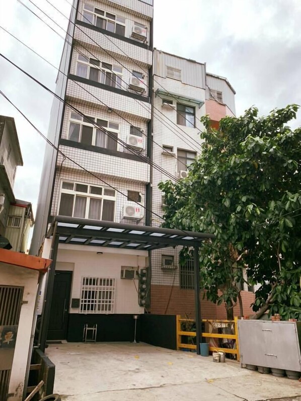 A multi-story residential building with a covered outdoor area, a tree, and a metal gate.