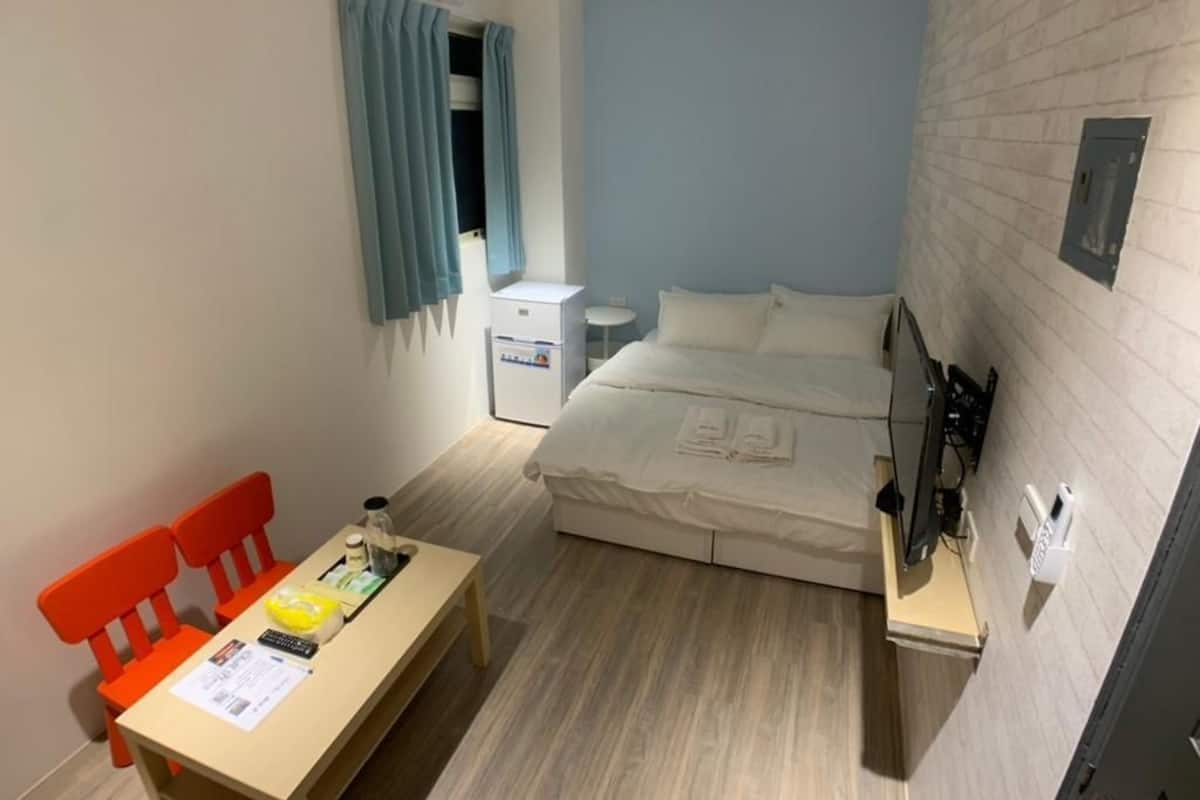 Une chambre d’hôtel de taille réduite, comprenant un lit, un petit bureau, une chaise et une fenêtre avec des rideaux.