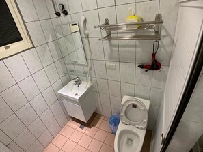 A small bathroom with a white sink, a toilet, and a mirror. There is a shelf above the toilet holding a yellow bottle and a red object.