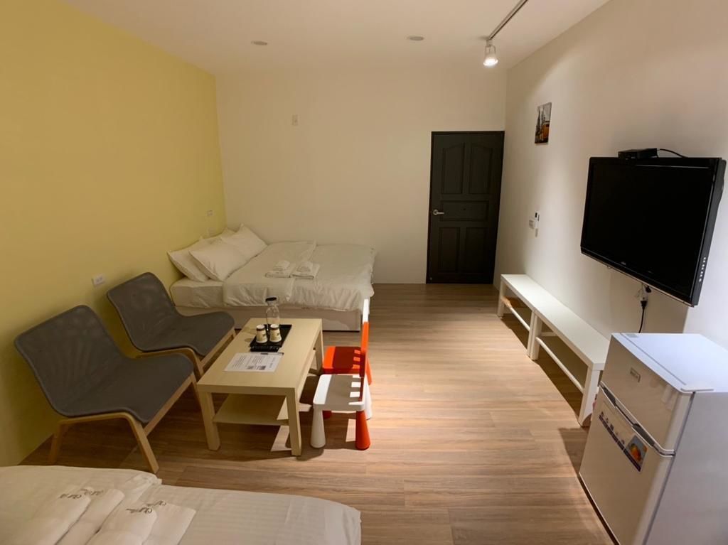 A compact hotel room with a bed, a sofa, a small table, a television, and a refrigerator.