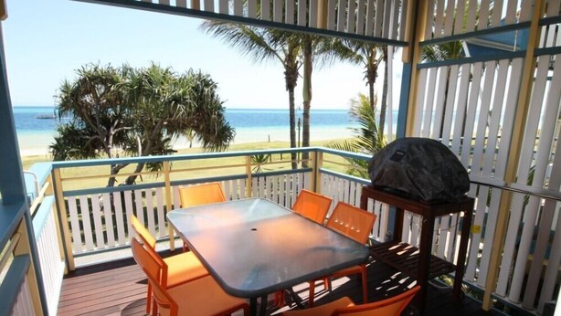 Un espace extérieur abrité, équipé d’une table et de chaises, d’un barbecue et offrant une vue sur la plage.