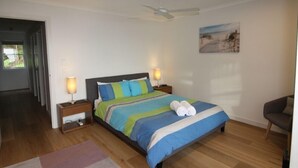 Une chambre à coucher comprenant un lit, des tables de chevet, un ventilateur de plafond, un tableau au mur et une chaise.