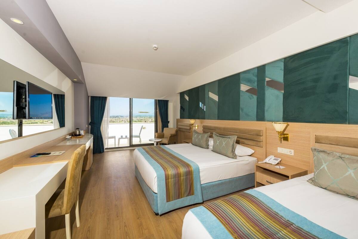 A hotel room with two beds, a desk, a chair, a TV, and a balcony with a view.