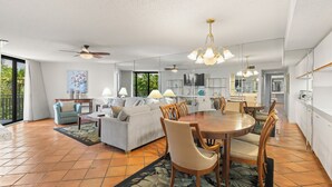 A spacious living area with a dining table, chairs, sofas, and a ceiling fan.