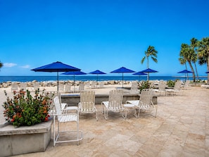 An outdoor seating area with chairs and umbrellas, a view of the ocean, and a stone-paved floor.