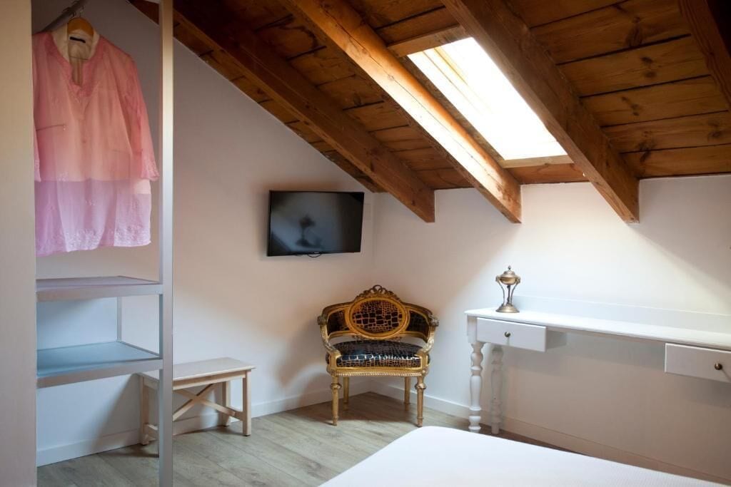 A bedroom with a wooden ceiling, a television mounted on the wall, a bench, and a bed.