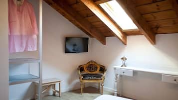 A bedroom with a wooden ceiling, a television mounted on the wall, a bench, and a bed.