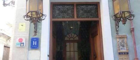A hotel entrance with a wooden door, ornate metal railings, and a sign indicating the hotel name.