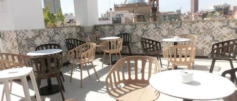 Una terraza en la azotea con varias mesas y sillas, una pared de azulejos con un diseño decorativo y vistas a un paisaje urbano que incluye una iglesia con cúpula y campanarios.