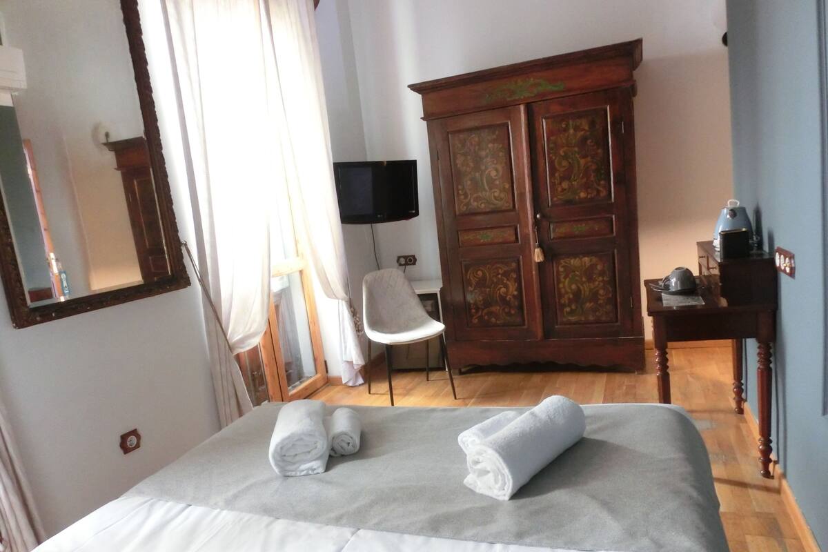 Een hotelkamer met een bed, een houten kledingkast, een stoel, een bureau en een televisie.