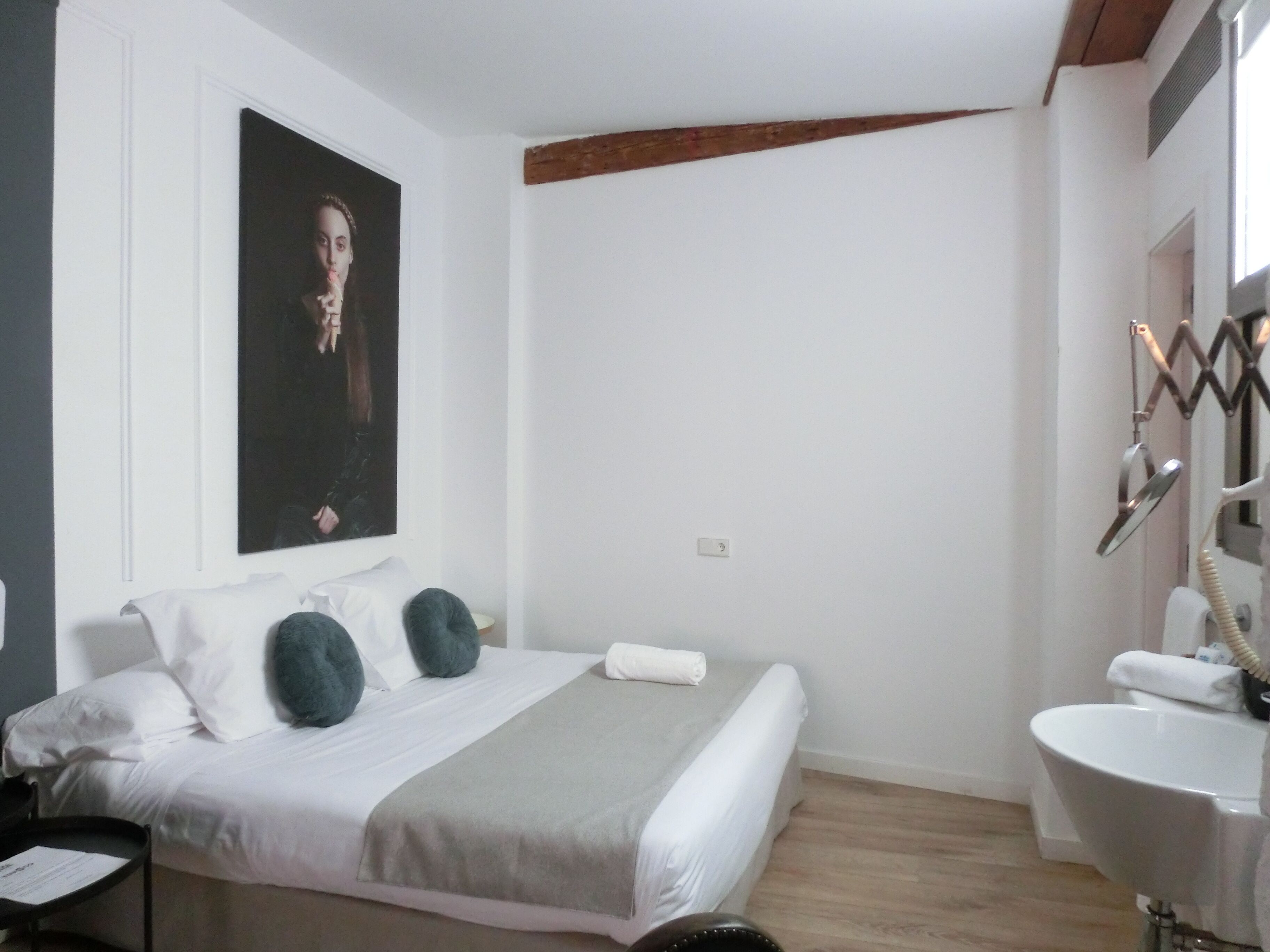 Une chambre à coucher avec un lit, des oreillers, une table de chevet et une affiche au mur, ainsi qu’une salle de bain avec un lavabo et un miroir.