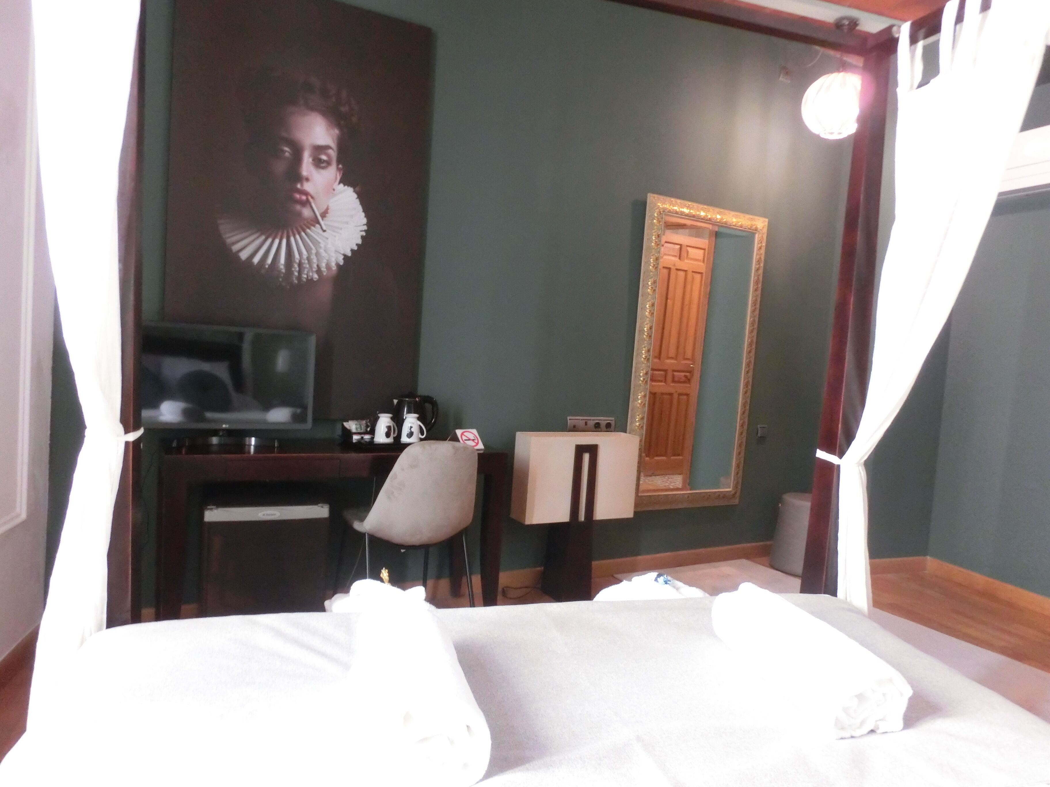 Habitación de hotel con cama, escritorio, silla, televisor, cafetera y espejo.
