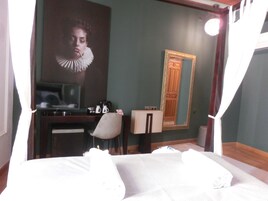Habitación de hotel con cama, escritorio, silla, televisor, cafetera y espejo.