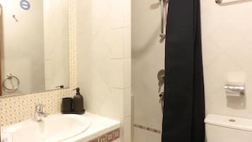 Un baño con lavamanos, espejo, ducha e inodoro.