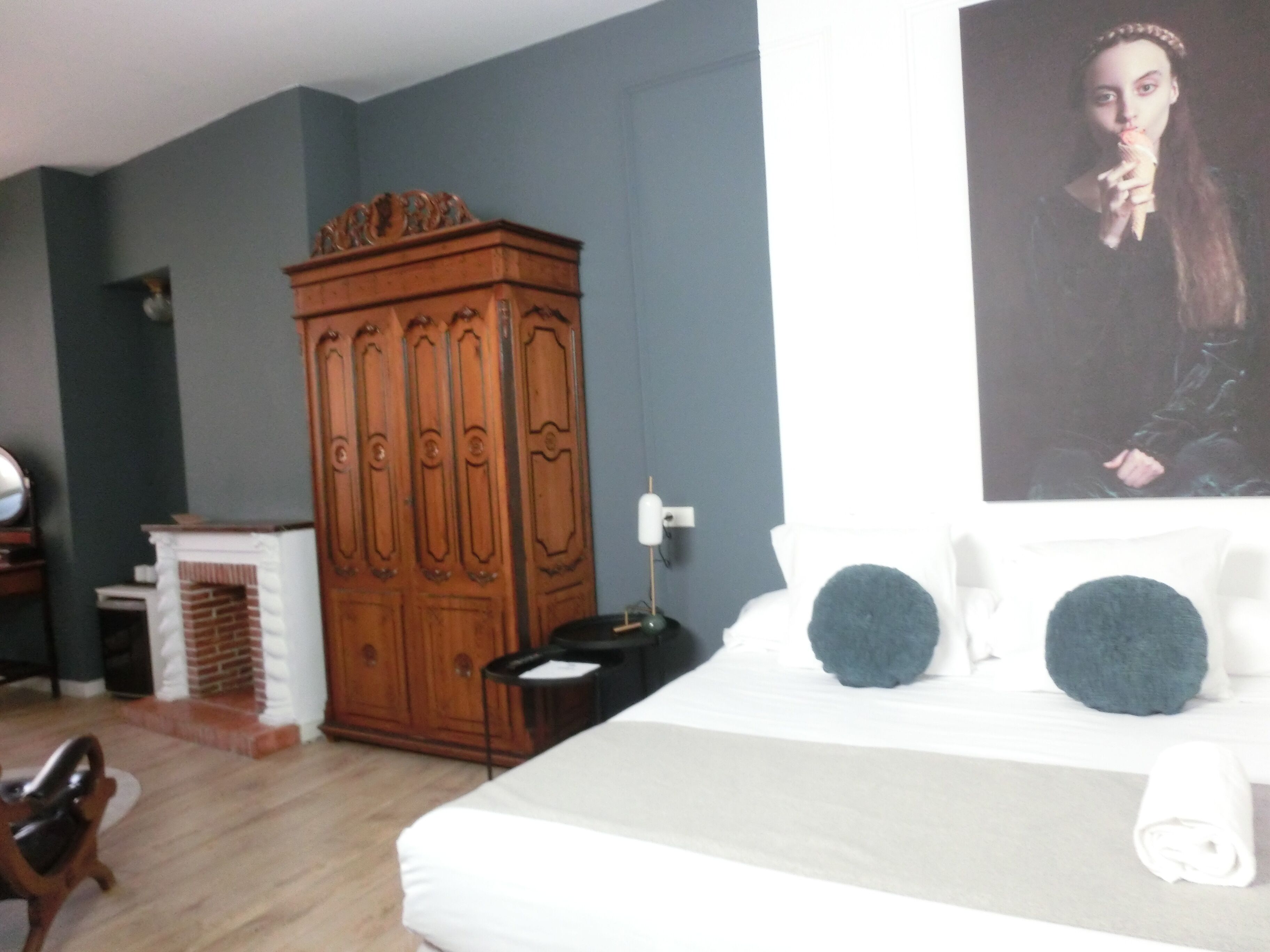 A bedroom with a large bed, a wooden wardrobe, a small table, and a wall-mounted picture.