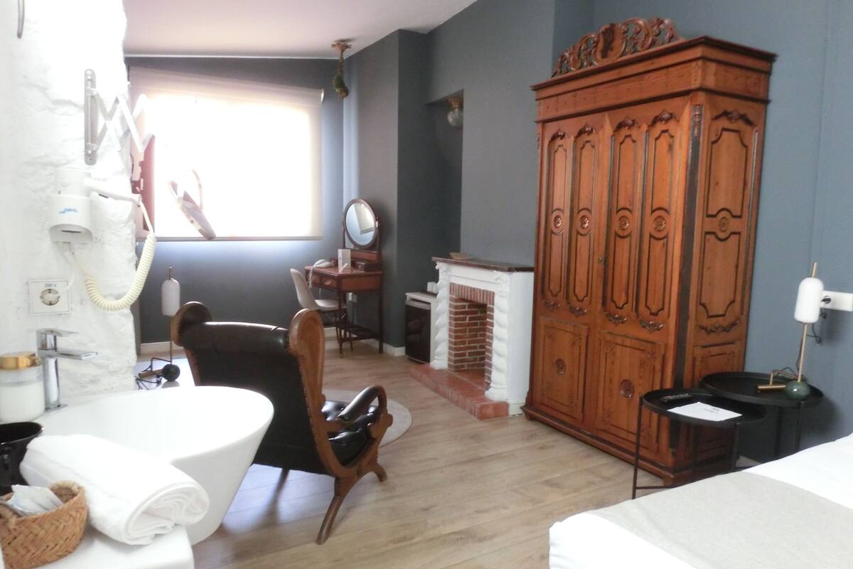 Een hotelkamer met een houten garderobe, een bureau met spiegel, een stoel, een witte wastafel en een bed.
