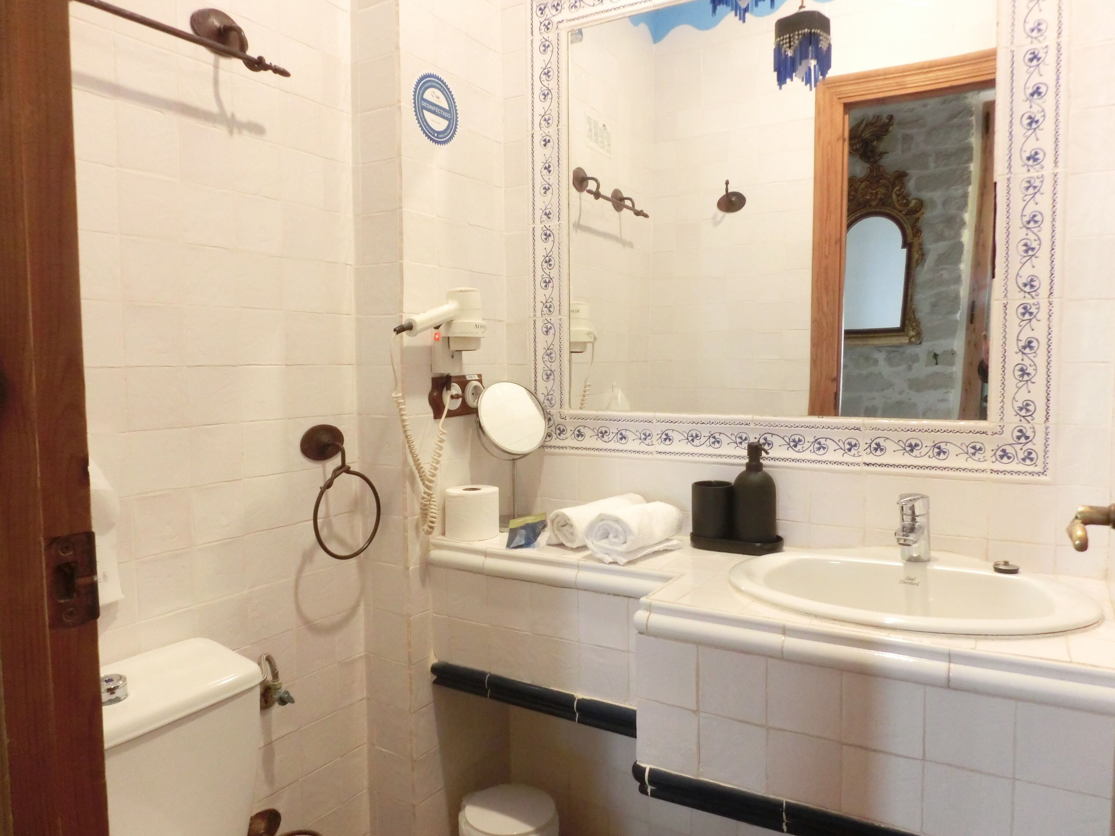 Une salle de bain équipée d’un WC, d’un lavabo et d’un miroir. On y trouve également un porte-serviettes, un sèche-cheveux et une bouteille de shampoing.