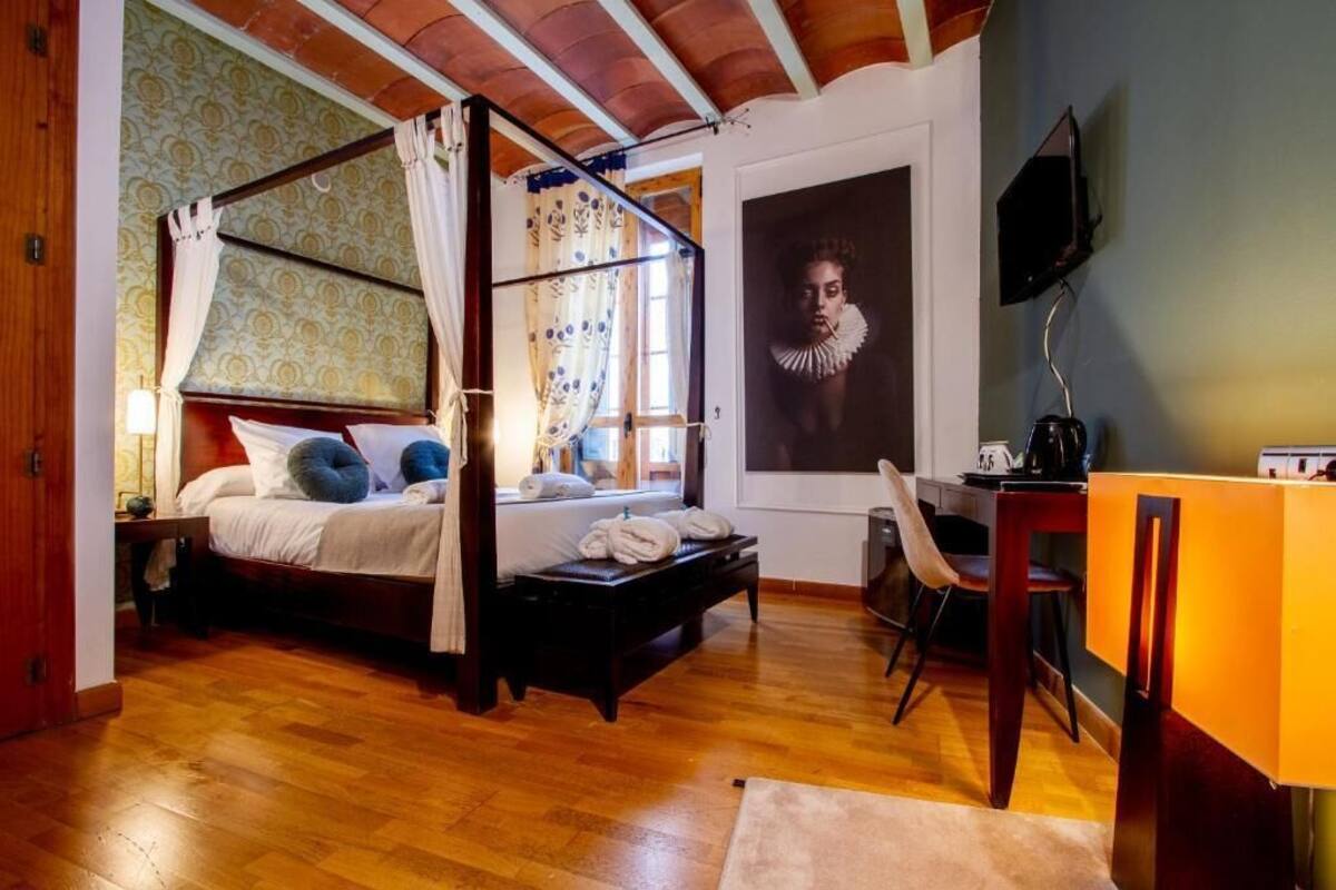 Een hemelbed met baldakijn, een bureau met stoel, een televisie en een groot portret in een lijst aan de muur.