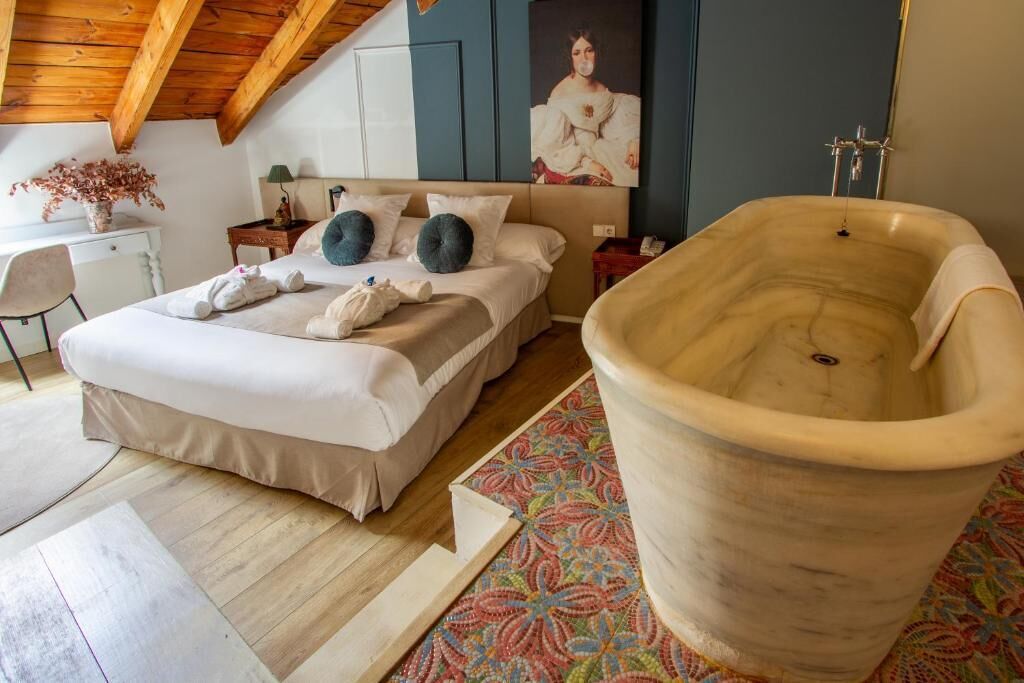 Quarto com uma banheira grande, cama com almofadas, escrivaninha e cadeira.