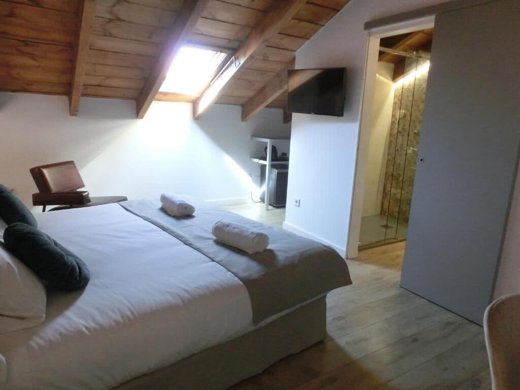 Quarto com cama grande, televisão fixada na parede e teto de madeira.