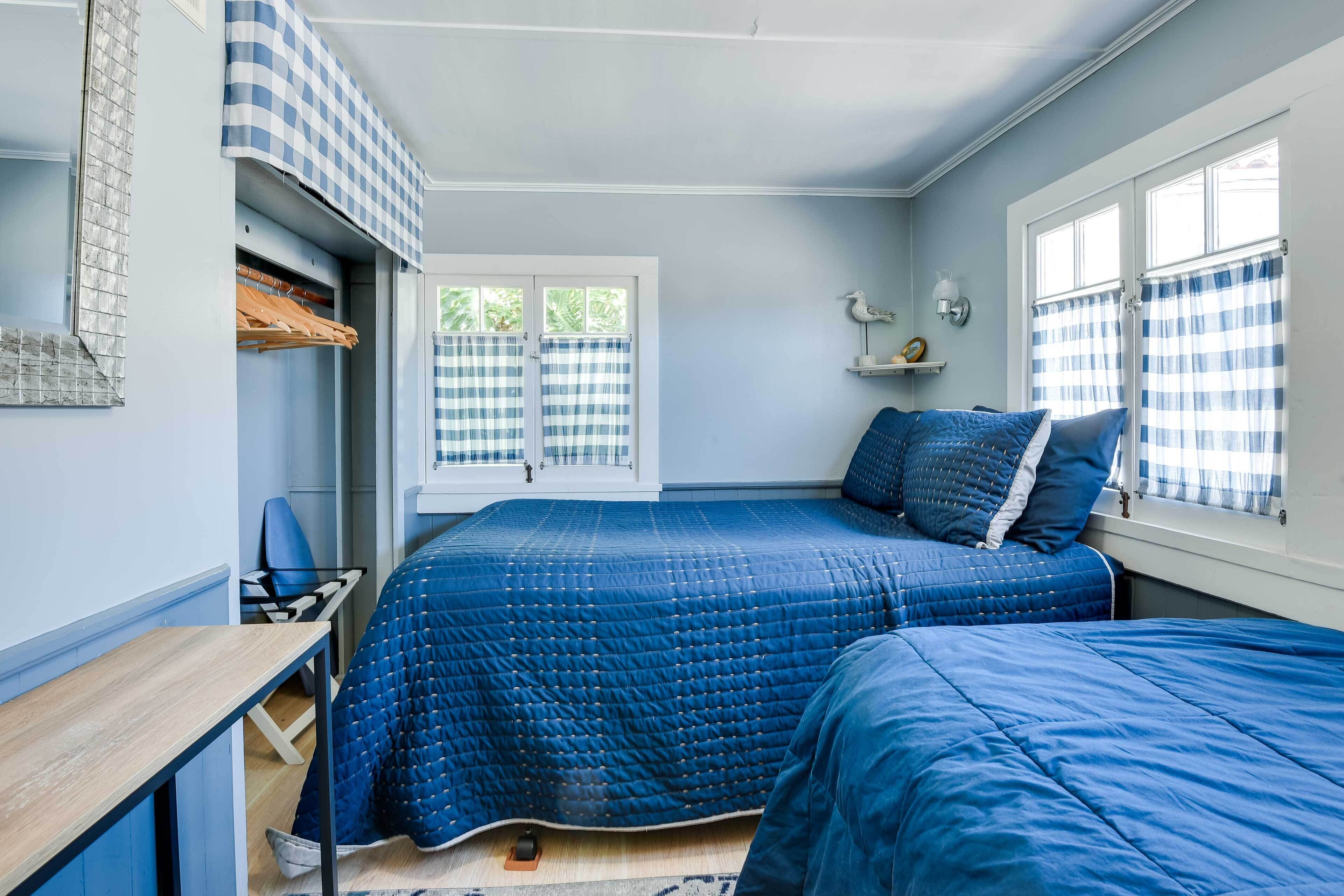 Un dormitorio con una cama acolchada azul, un escritorio de madera, una silla y una ventana con cortinas a cuadros.