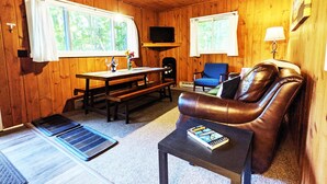 A cozy cabin interior with wooden walls, a leather couch, a dining table with chairs, and a television mounted on the wall. - Amenities & Resort Access Included, Cabin 5 (Phelps)