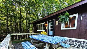 A wooden deck with checkered picnic tables and benches, surrounded by a forest. - Amenities & Resort Access Included, Cabin 5 (Phelps)