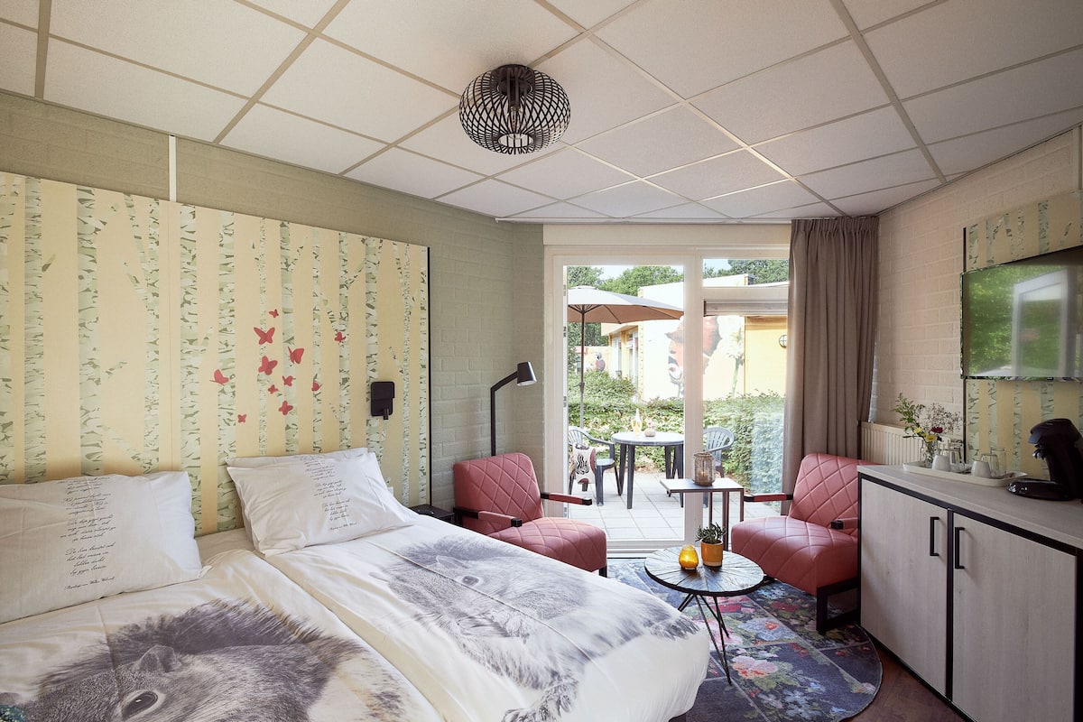 A hotel room with a bed, a desk, a chair, and a small table with a plant.