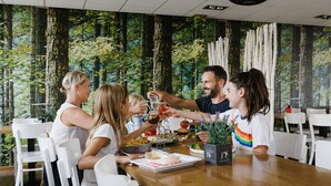 Un groupe de personnes est assis à une table en bois dans une pièce dont un des murs est décoré d’une fresque représentant une forêt.