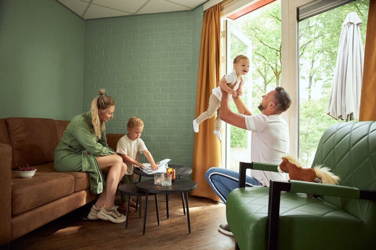 A family in a living room with a green couch, a small round table, and a window with curtains.
