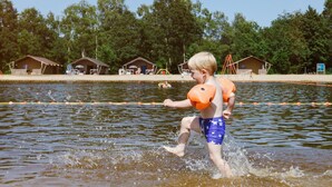 Un enfant joue dans une étendue d’eau délimitée par des barrières flottantes.