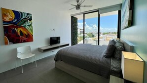 Un dormitorio moderno con una cama grande, un televisor, una silla blanca y un cuadro en la pared.