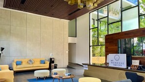 Un vestíbulo moderno con recepción, zona de estar y amplios ventanales que ofrecen vistas al verdor.