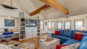 Un salon spacieux avec un canapé bleu, des meubles en osier blancs et une poutre en bois au plafond.
