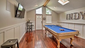 A pool room with a pool table, a television mounted on the wall, and a door leading to another room. - Updated Indianapolis Home, Walk to Lucas Oil! (Indianapolis)
