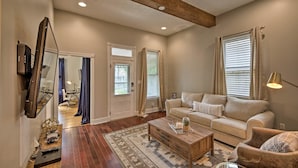 A spacious living room with a wooden coffee table, beige sofa, and a TV mounted on the wall. - Updated Indianapolis Home, Walk to Lucas Oil! (Indianapolis)