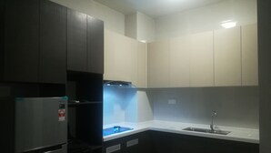 Cozinha compacta com armários escuros, geladeira de aço inoxidável, forno embutido e pia.