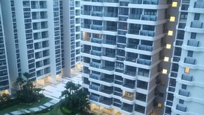 Um edifício residencial alto, com várias varandas, um pátio central com área de recreação circular e áreas verdes ao redor.